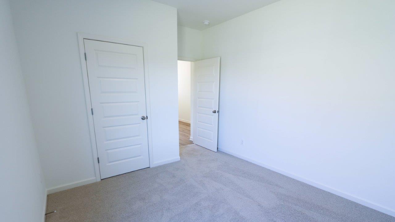 Empty room with two closed white doors and beige carpet flooring.