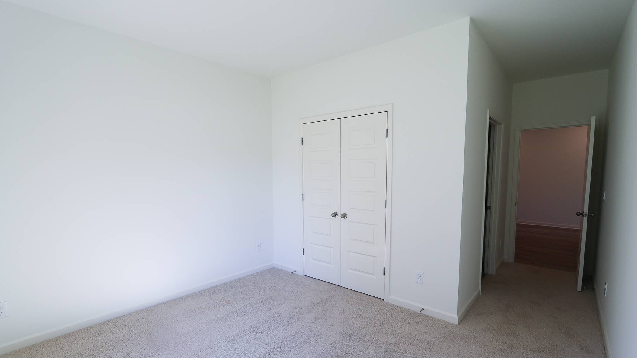 Empty room with beige carpet, white walls, and a closed white door.