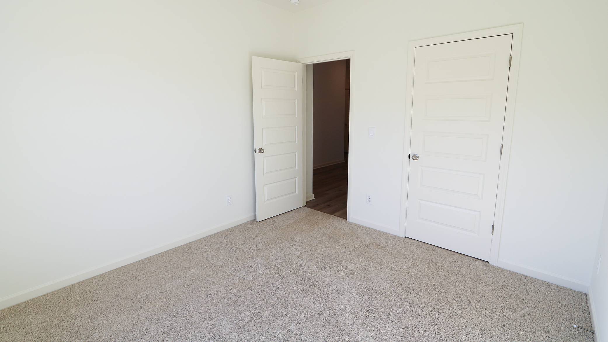 Empty room with beige carpet, white walls, and two closed white doors.