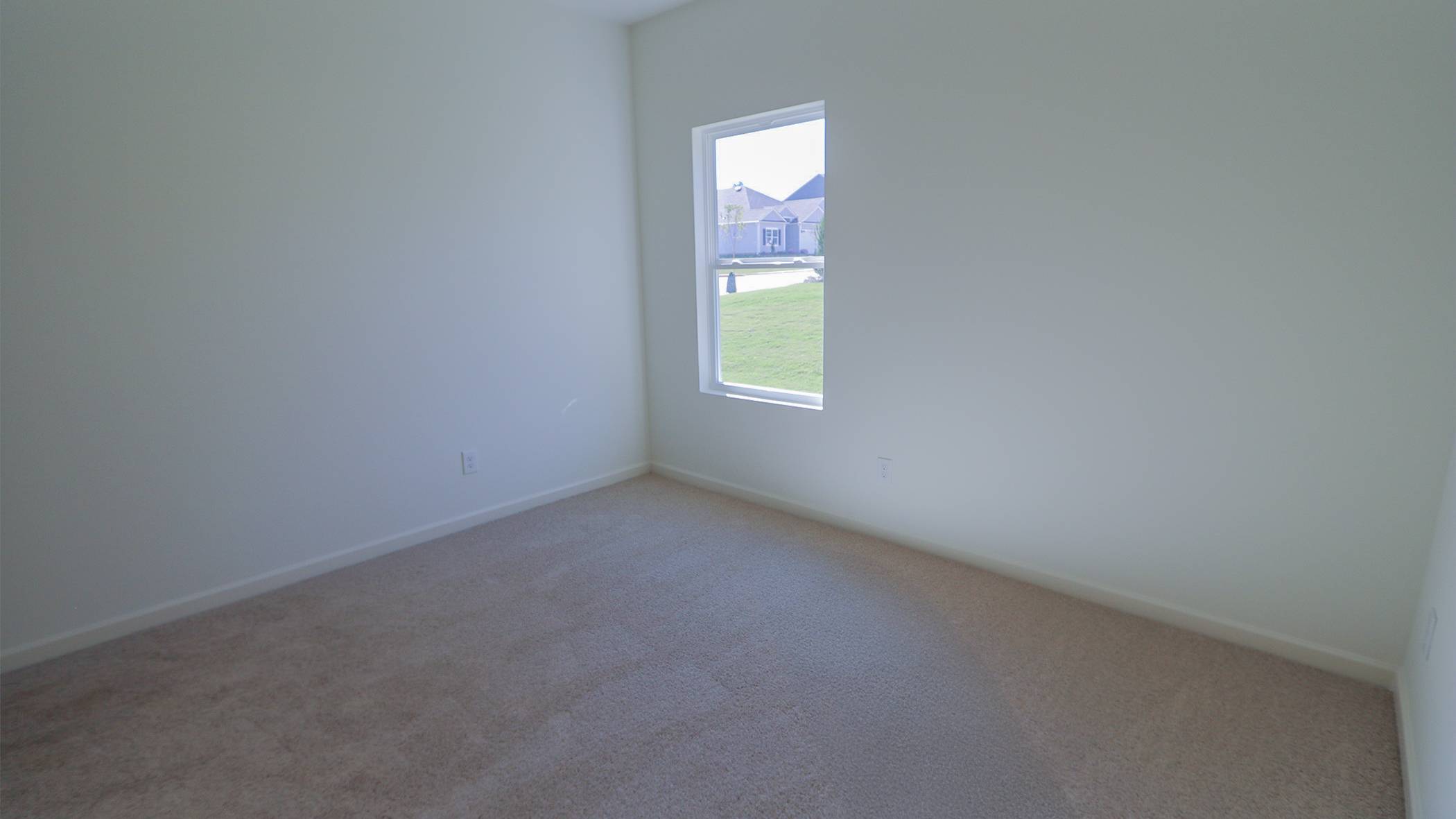 Empty room with beige carpeting, white walls, and a single window with a view of a lawn outside.