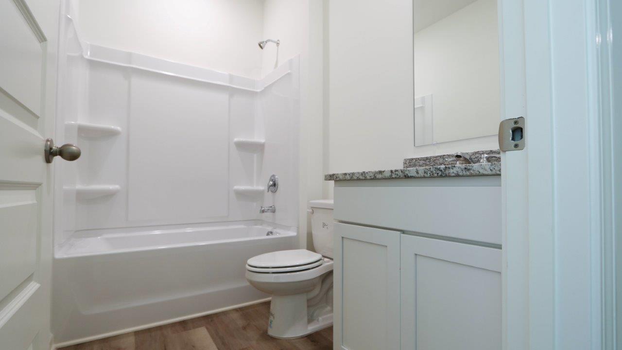 Modern bathroom with white tub/shower combo, toilet, and vanity.