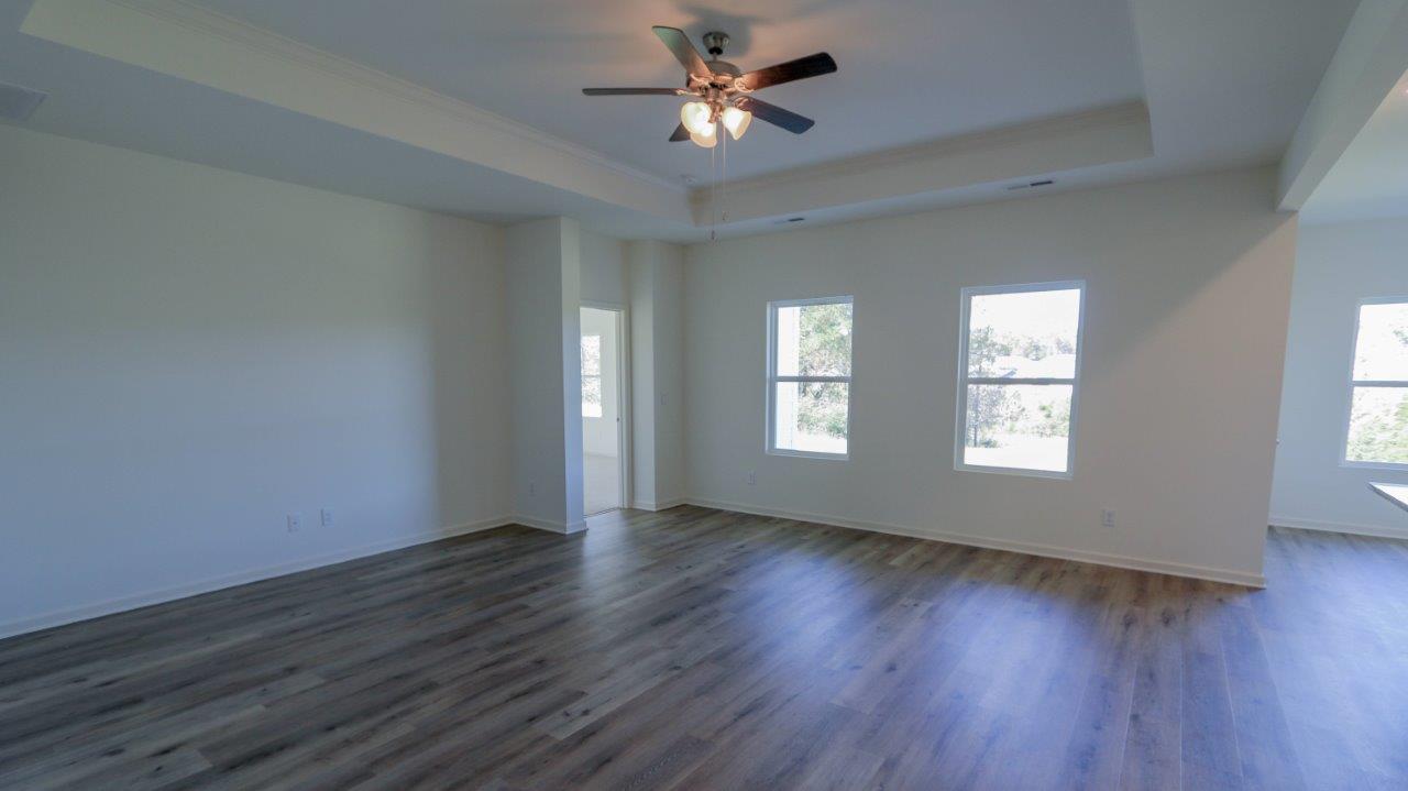 Empty room with hardwood floors, white walls, ceiling fan, and three windows.