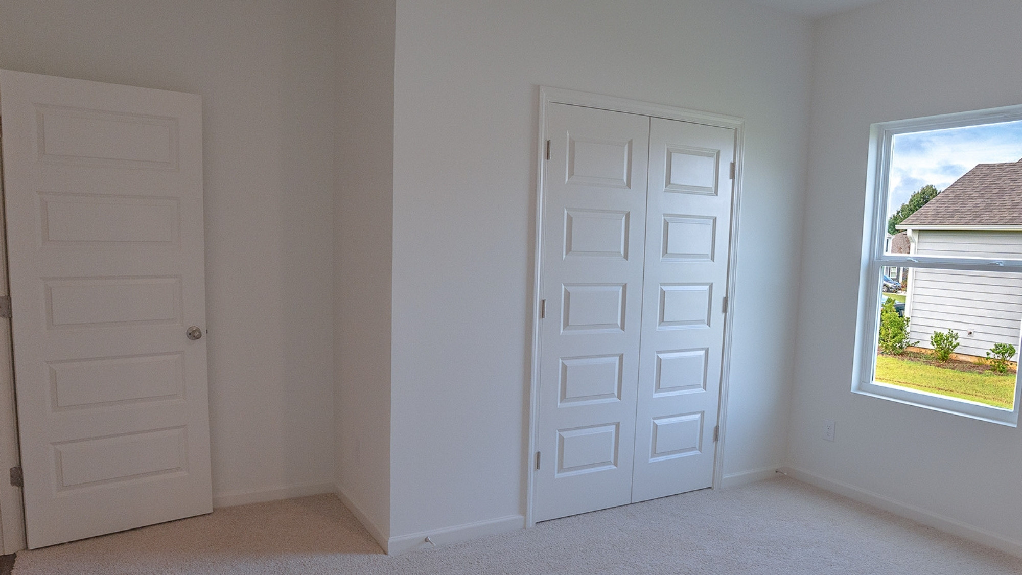 Spacious bedroom featuring a bed, two nightstands, and a closet, with large windows and carpeted floors for a warm, inviting feel.
