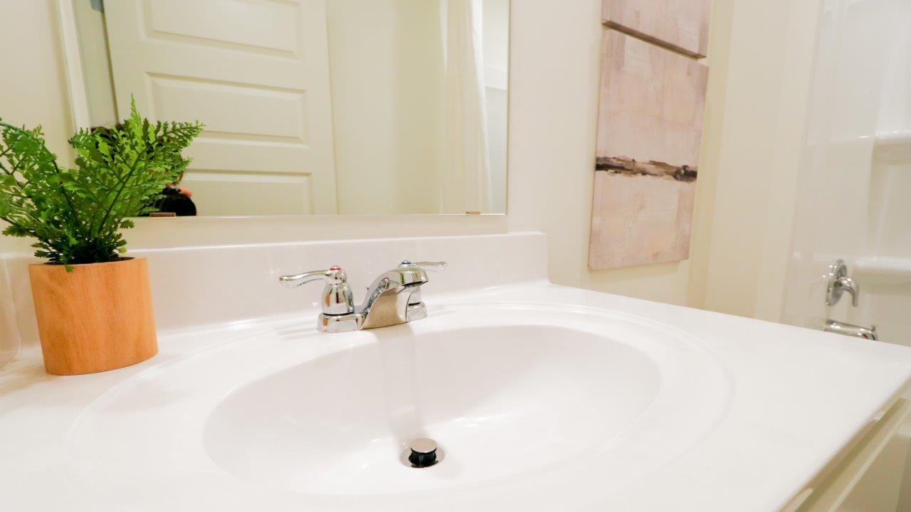 The bathroom is comprised of a tub/shower, toilet, and vanity. The walls are white, and the floors are made of wood, which gives the space a clean and natural aesthetic.