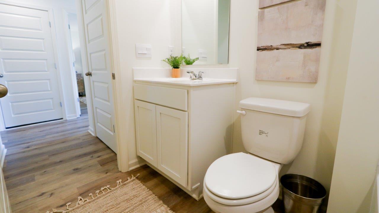 The bathroom is comprised of a tub/shower, toilet, and vanity. The walls are white, and the floors are made of wood, which gives the space a clean and natural aesthetic.