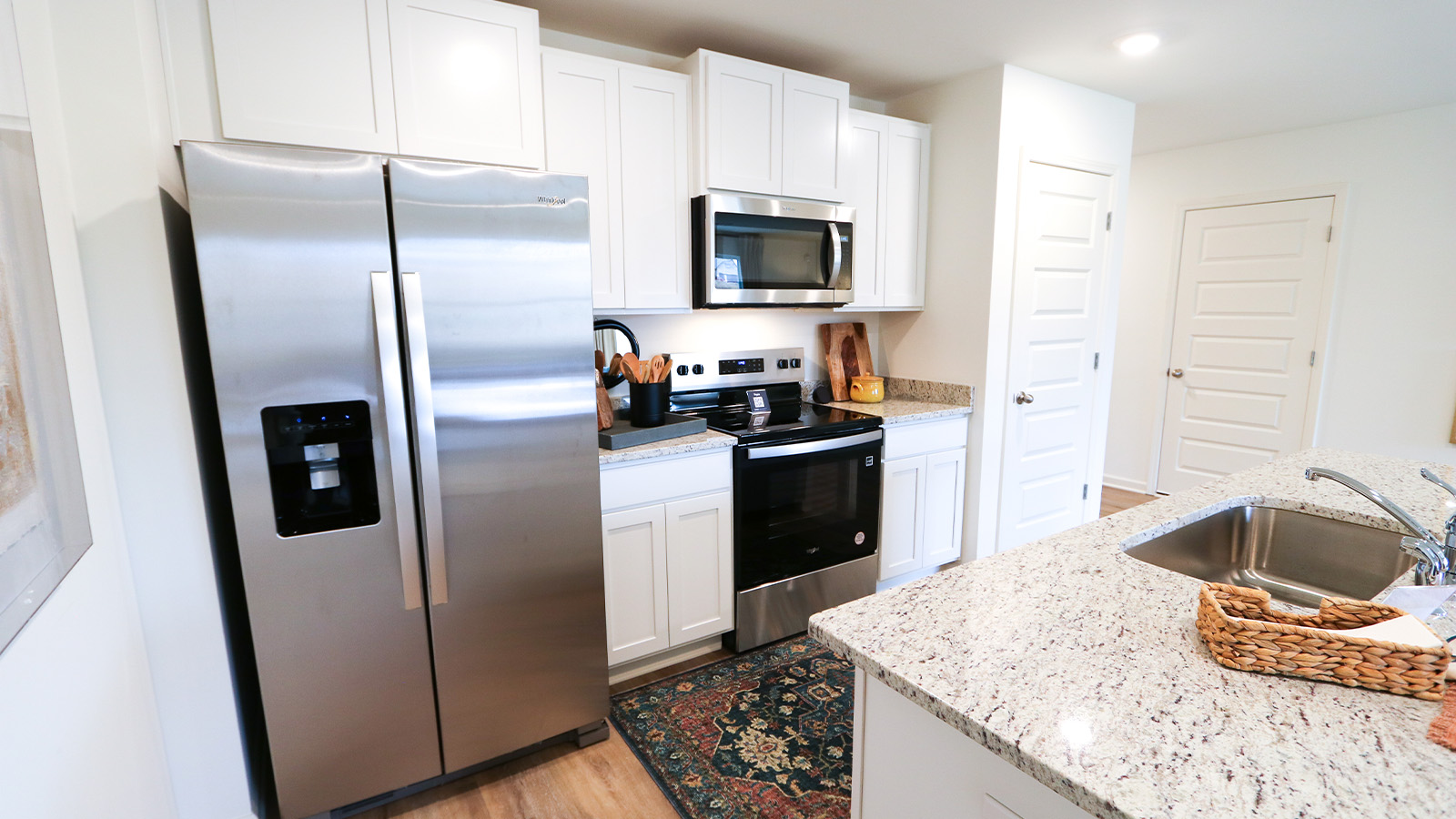 An open concept kitchen that opens to the dining room and the living room features an oversized kitchen island with 3 barstools, stainless steel appliances, white cabinets and a pantry.