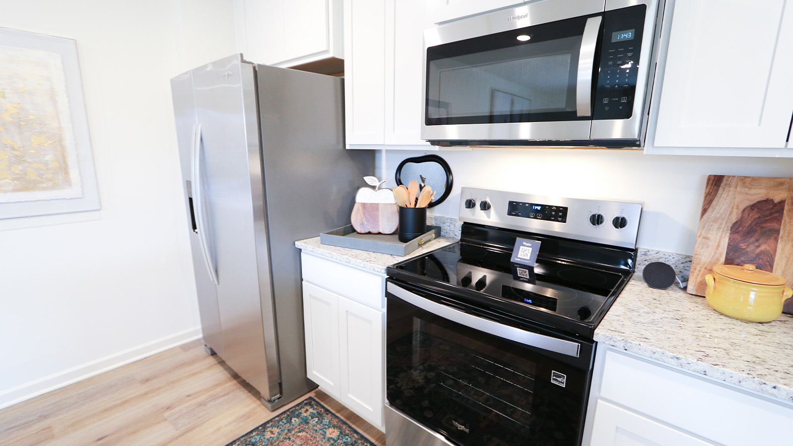 An open concept kitchen that opens to the dining room and the living room features an oversized kitchen island with 3 barstools, stainless steel appliances, white cabinets and a pantry.