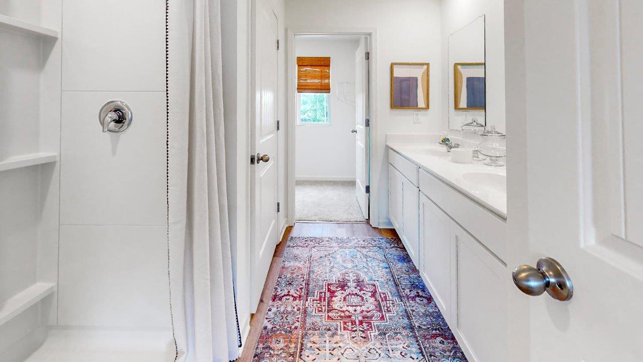 A modern bathroom with white cabinets, double vanities, and a shower located on the left side of the space