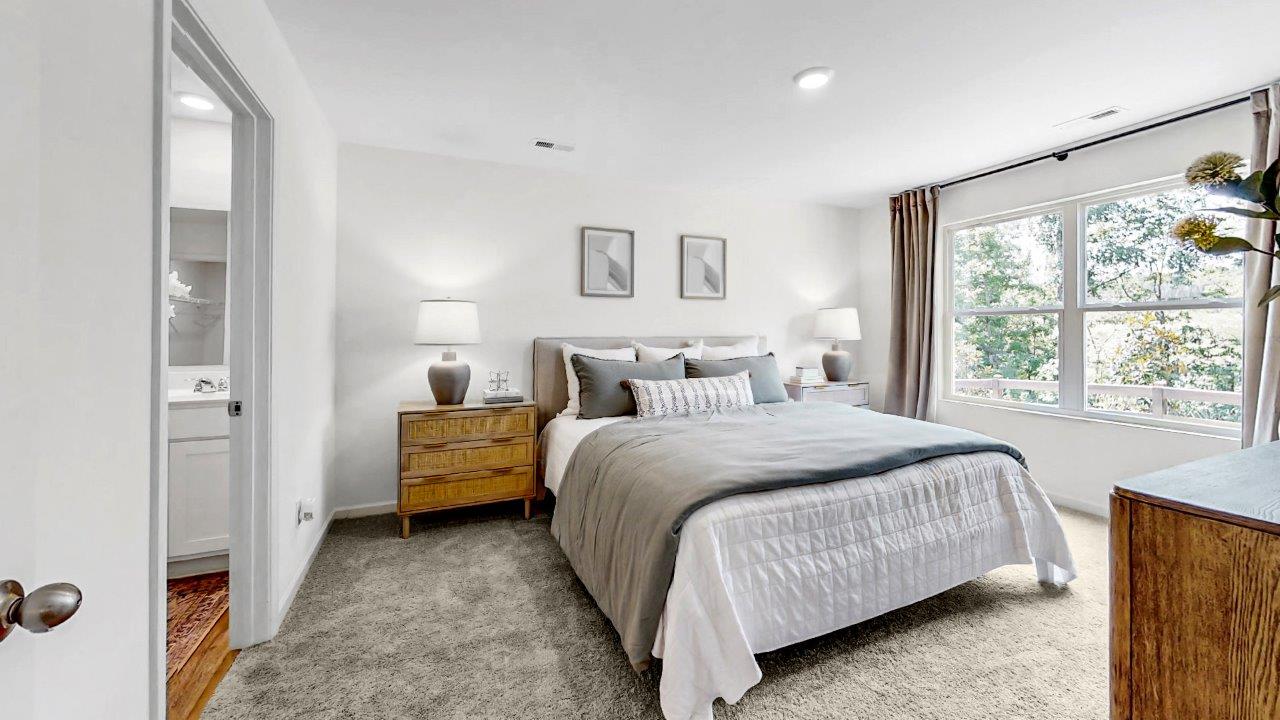 The spacious primary bedroom features a generously sized king bed, two nightstands, and a large double window with a view of the backyard. The room offers ample space for comfortable movement and relaxation.