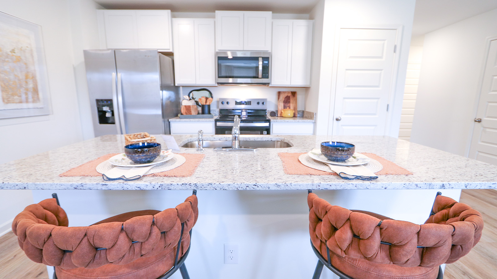 The open concept kitchen is designed to seamlessly connect with the dining room and the living room. It showcases an oversized kitchen island equipped with three barstools for seating. The kitchen is furnished with stainless steel appliances, white cabinets, and a pantry for storage.