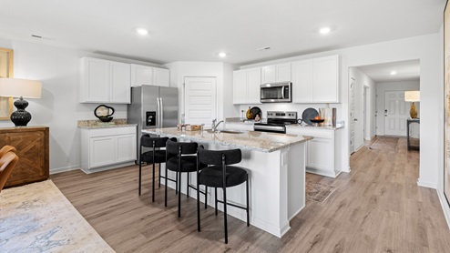 The kitchen is a spacious open concept area with stainless steel appliances. It includes an oversized kitchen island with barstools for seating and food preparation. Additionally, there is a convenient walk-in pantry for storage.