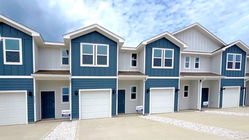 Exterior elevation of new townhomes with dark blue siding and white trim,