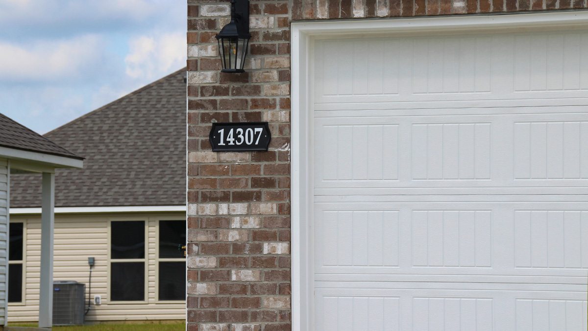 Single-story home with brown brick. Black glass front door with black shutters and white trim.
