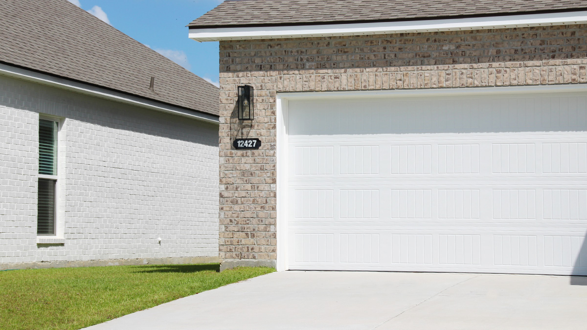 two-story home with tan brick and light gray vinyl siding with gray front door and shutters with porch and two-car garage