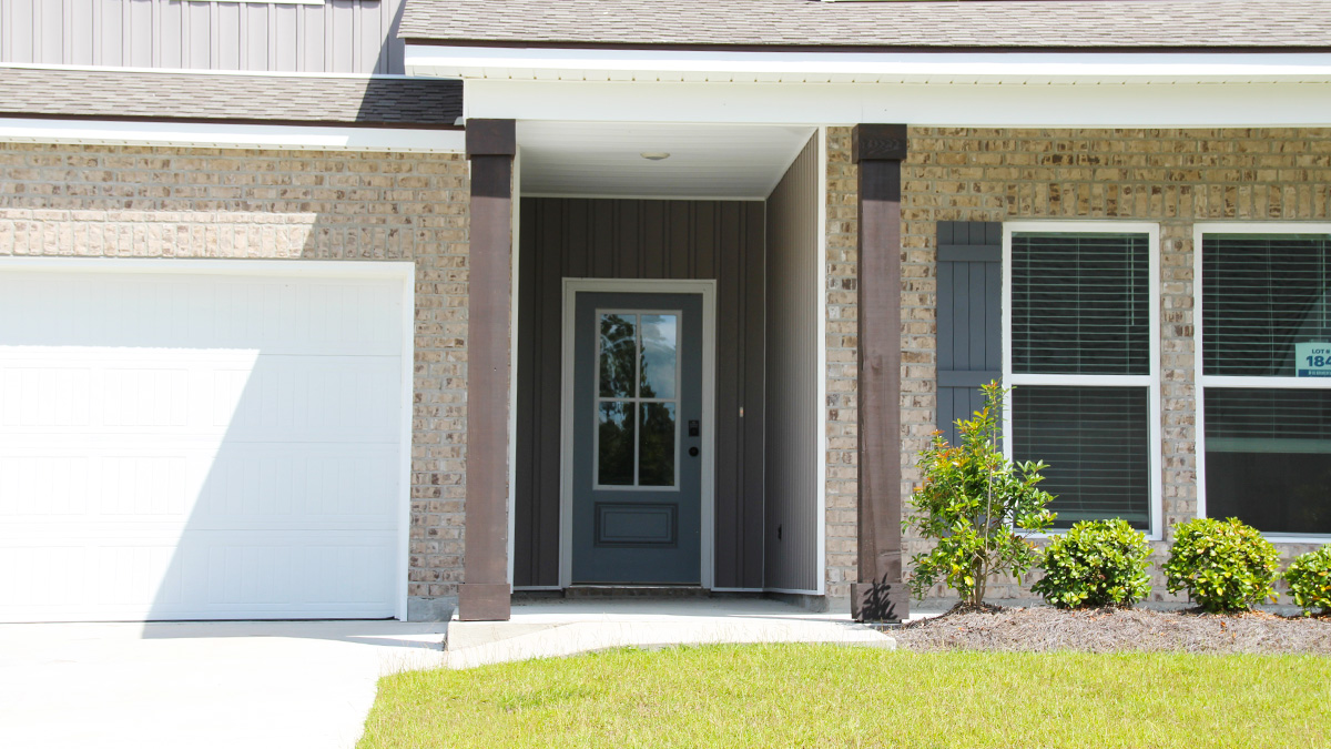 two-story home with tan brick and light gray vinyl siding with gray front door and shutters with porch and two-car garage