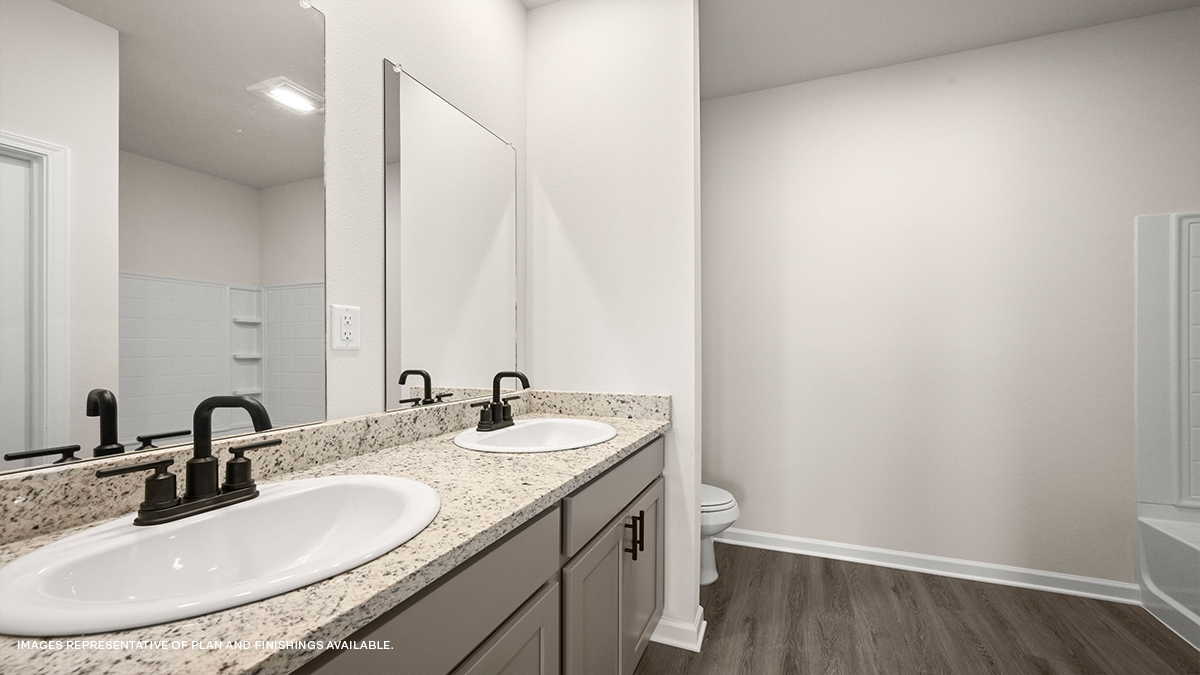Tan dual vanities with toilet in the rear with shower tub combo in the primary bath