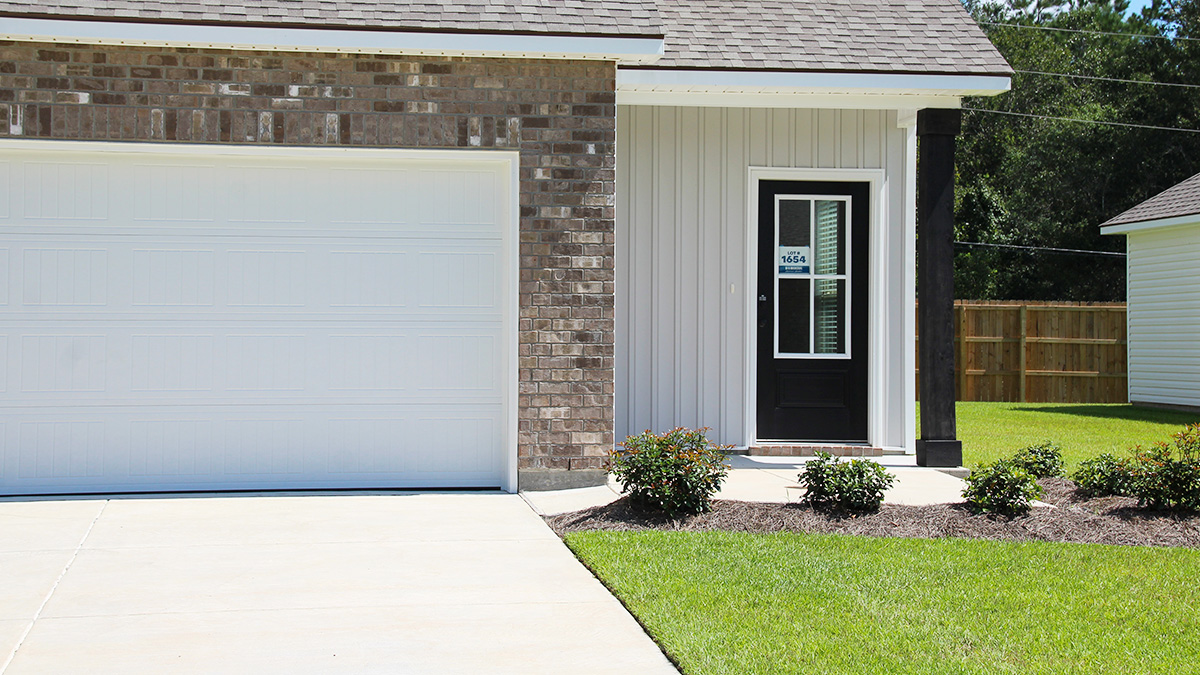 Two-story home with grey hardie vinyl and brown brick. Navy blue glass front door with navy blue shutters.