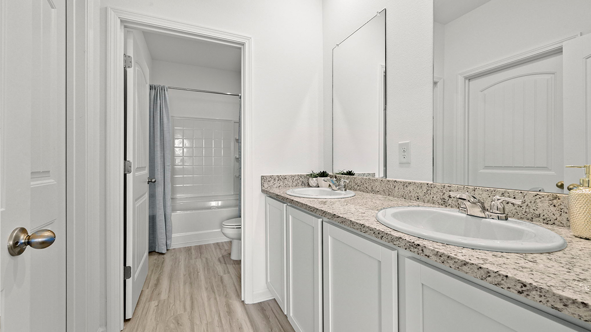 primary bathroom with dual vanities and opening to shower tub combo and toilet space