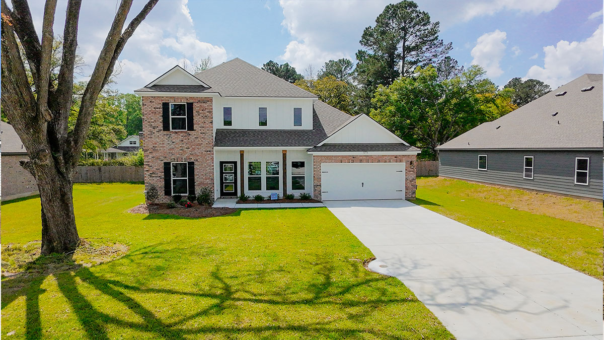 double-story home with tan brick and white vinyl siding with black front door and shutters with porch and two-car garage