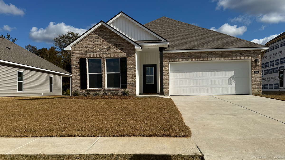 single-story home with tan brick and grey vinyl siding with black front door and shutters with two-car garage