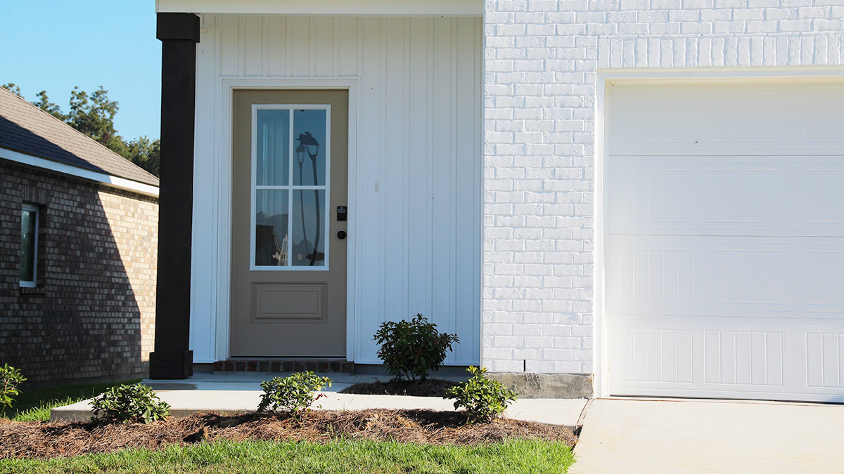 Two-story home with white hardie vinyl and white brick. Tan glass front door with tan shutters and white trim.