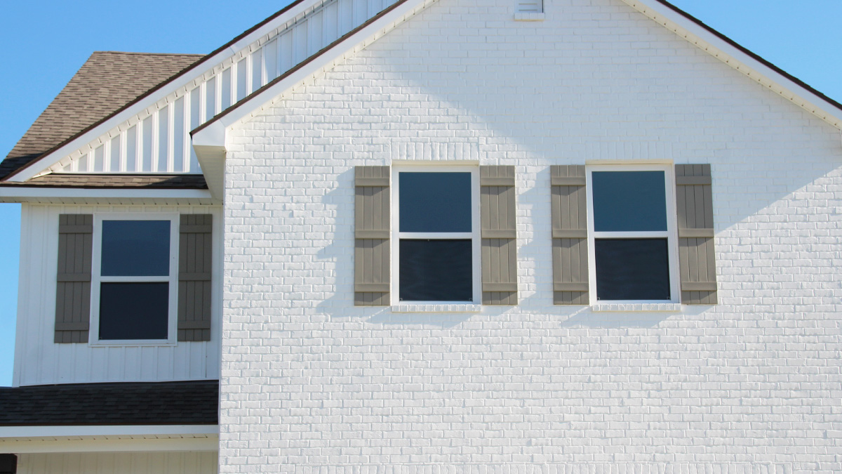 Two-story home with white hardie vinyl and white brick. Tan glass front door with tan shutters and white trim.