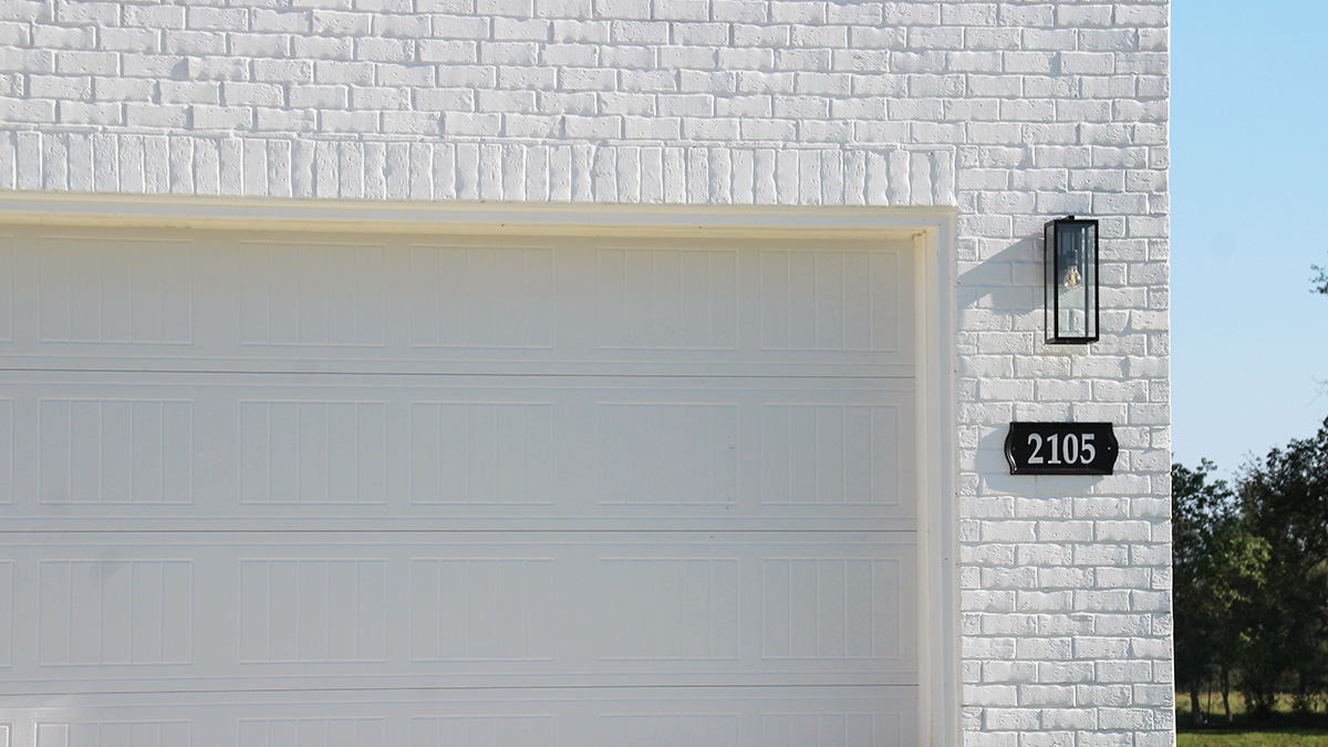 Two-story home with white hardie vinyl and white brick. Tan glass front door with tan shutters and white trim.