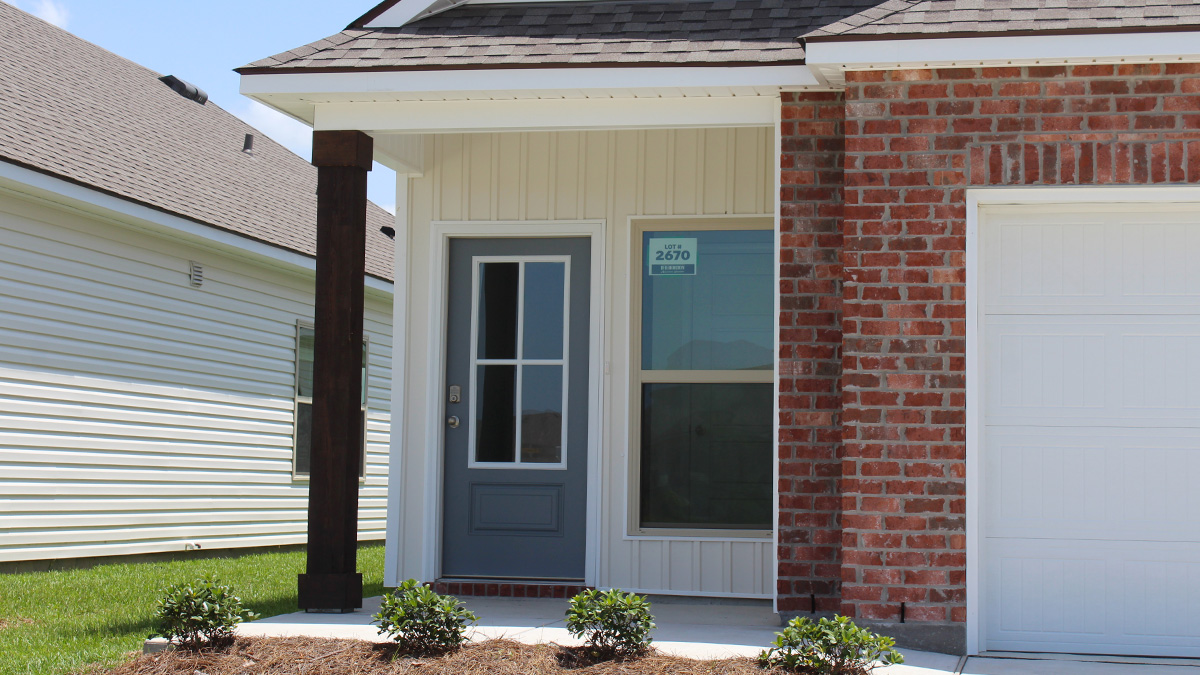 Single-story home with red brick. Blue glass front door with white hardie vinyl and white two car garage.