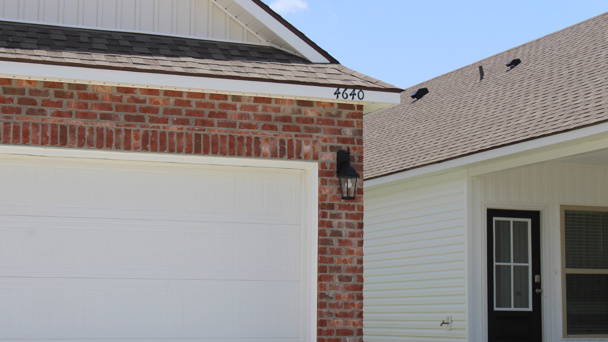 Single-story home with red brick. Blue glass front door with white hardie vinyl and white two car garage.