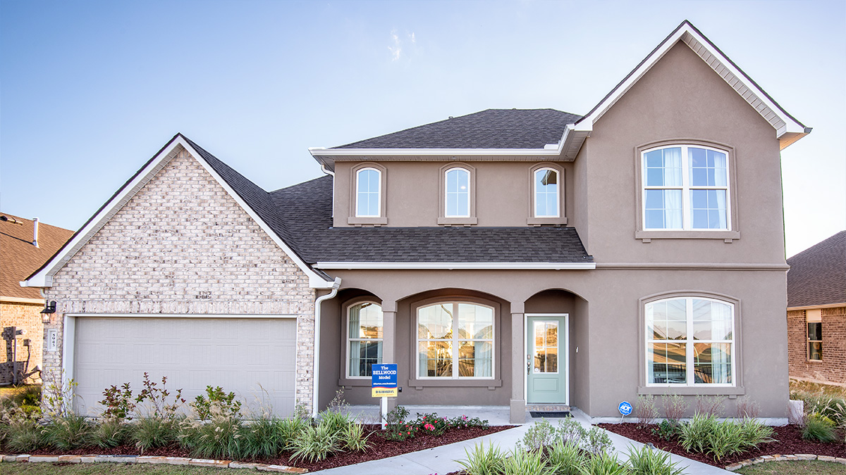 double-story home with tan stucco siding and light brown brick with porch and two-car garage
