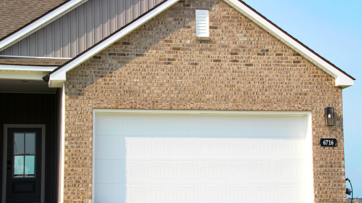 Single-story home with tan brick and tan hardie vinyl. Black glass front door and white two car garage.
