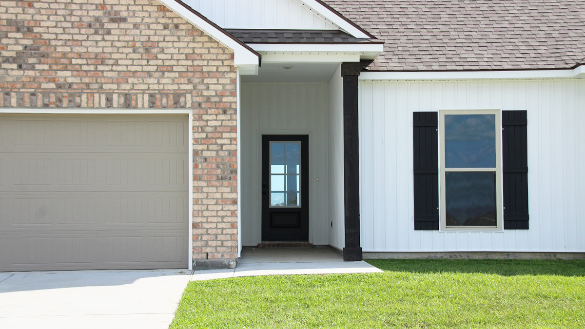 Single-story home with brown brick. Black glass front door with black shutters and white trim.
