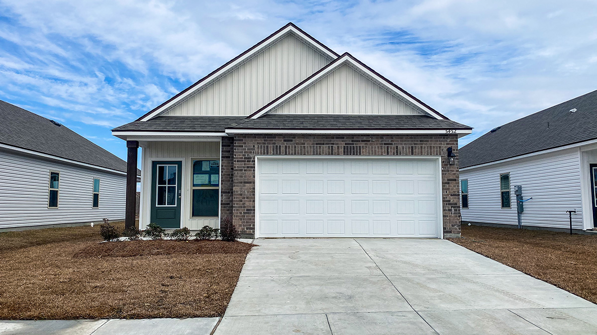 single-story home with brown brick and tan vinyl siding with blue-green front door and small porch with two-car garage