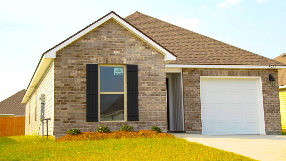 Single-story home with brown brick. Black glass front door with brown shutters and white one car garage.