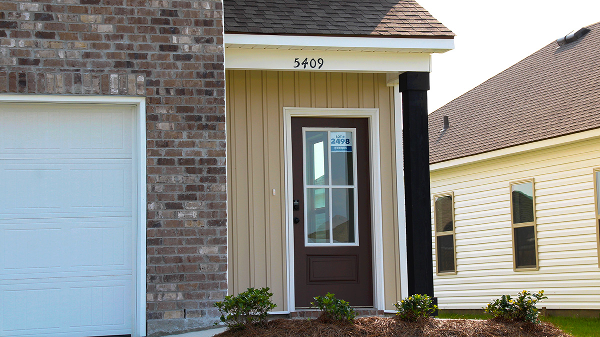 Two-story home with cream hardie vinyl and brown brick. Brown glass front door with brown shutters and white two car garage.