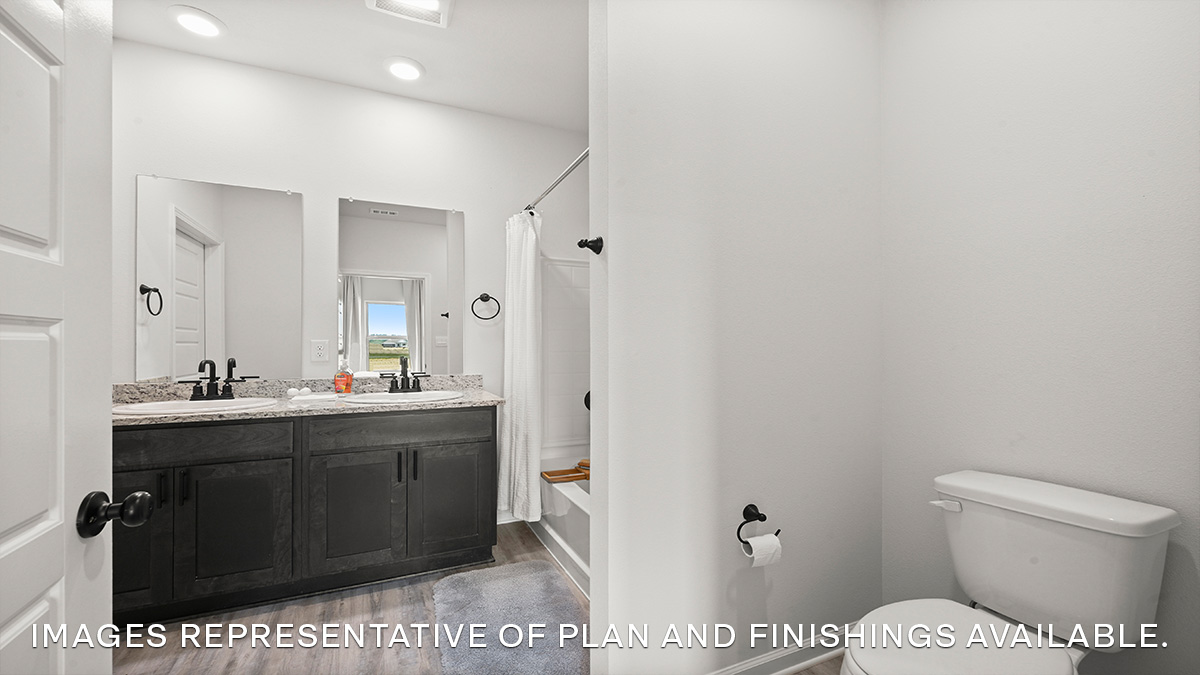 Toilet area in the primary bathroom with dual vanities and shower tub combo in the rear