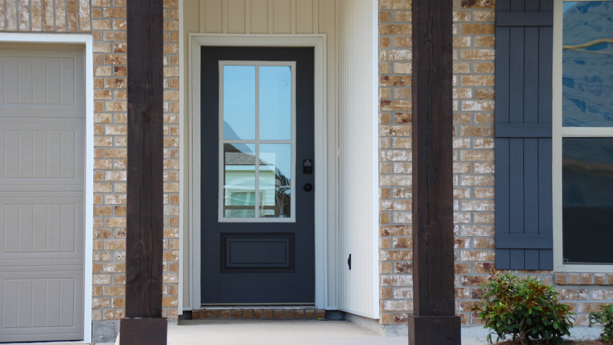 Single-story home with brown brick. Dark grey glass front door with dark grey shutters and white trim.