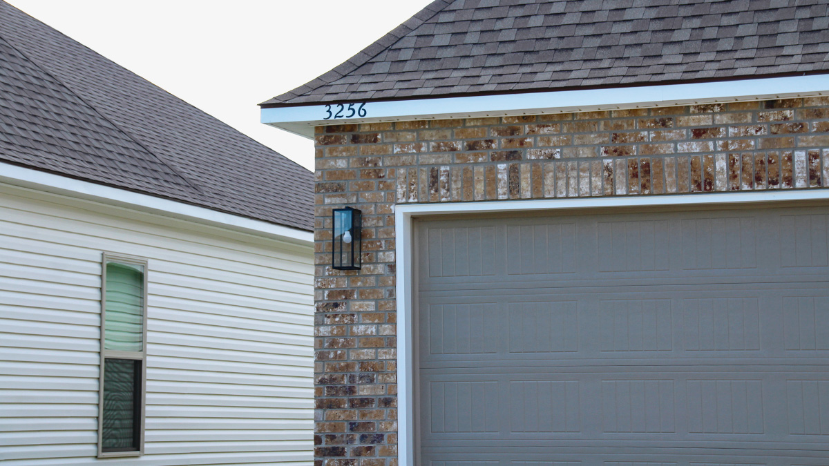 Single-story home with brown brick. Dark grey glass front door with dark grey shutters and white trim.