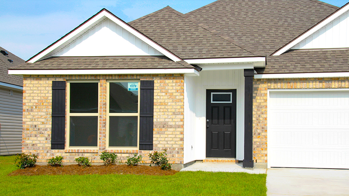 Single-story home with tan brick. Black glass front door with black shutters and white two car garage.