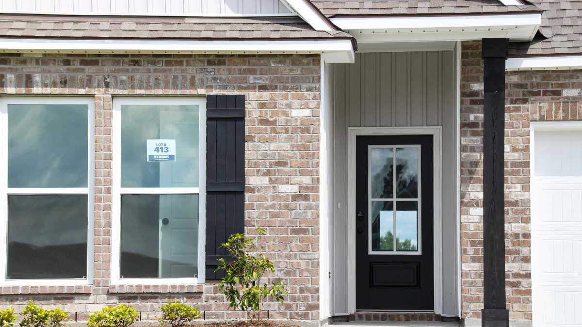 Single-story home with brown brick. Black glass front door with black shutters and white trim.