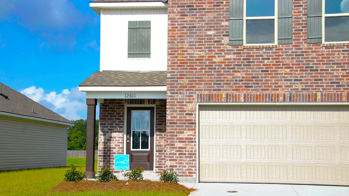 Two-story home with white hardie vinyl and red brick. Brown glass front door with grey shutters and tan two car garage.