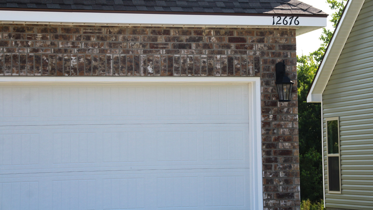 Single-story home with brown brick. Tan glass front door with black posts and white two car garage