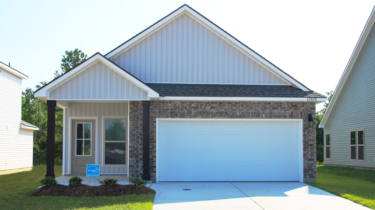 Single-story home with brown brick. Tan glass front door with black posts and white two car garage