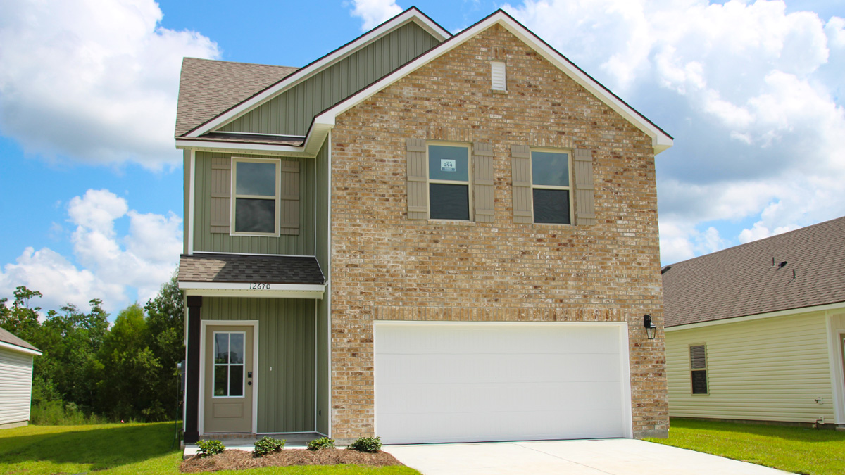 Two-story home with green hardie vinyl and tan brick. Tan glass front door with tan shutters and white trim.