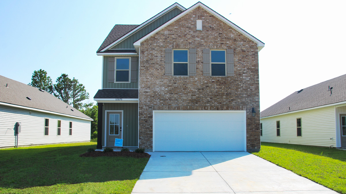 two story home with tan brick. Tan glass door and tan shutters. Green vinyl and white two car garage and long driveway.