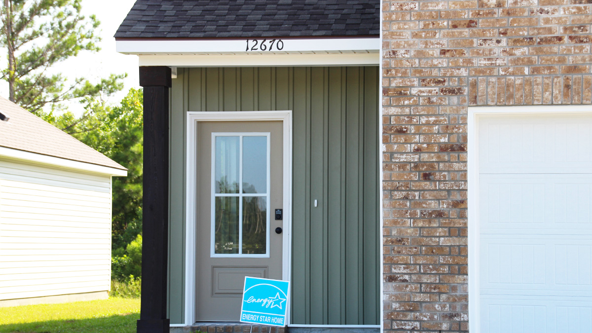 two story home with tan brick. Tan glass door and tan shutters. Green vinyl and white two car garage and long driveway.