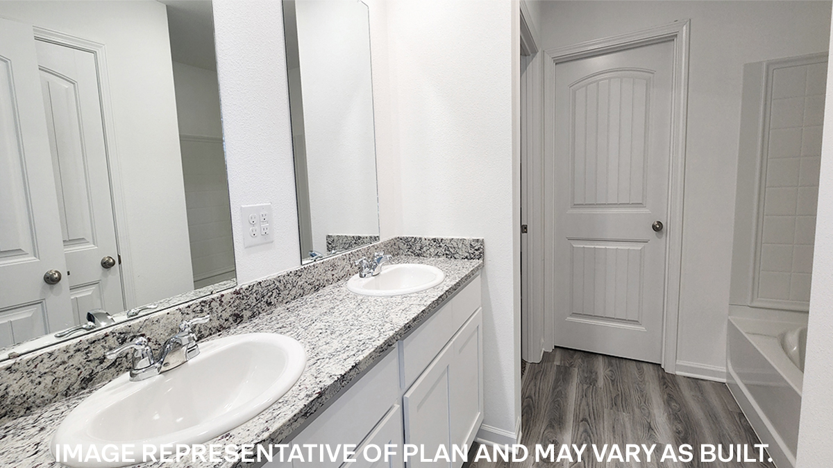 primary bathroom with dual vanities and opening to walk in closet