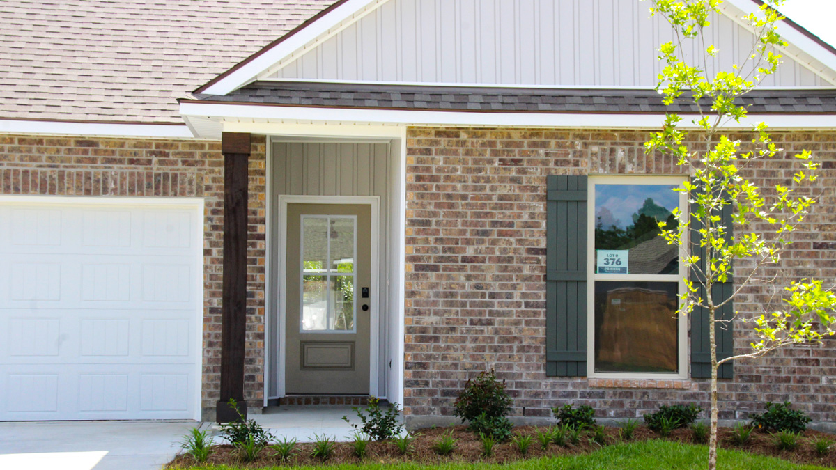 Single-story home with brown brick. Tan glass front door with dark grey shutters and white trim.