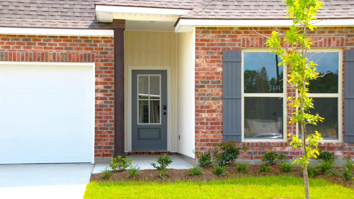 Single-story home with red brick. Blue glass front door with blue shutters and white two car garage.