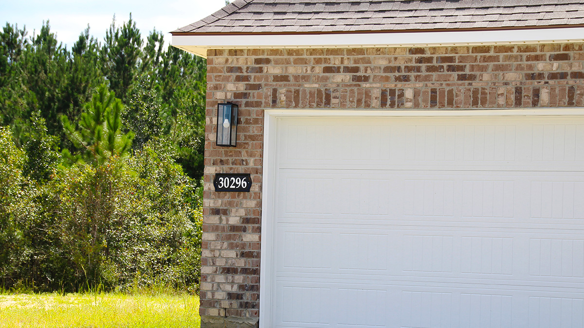 single-story home with tan brown brick with tan vinyl siding with bleck front door and shutters with two-car garage